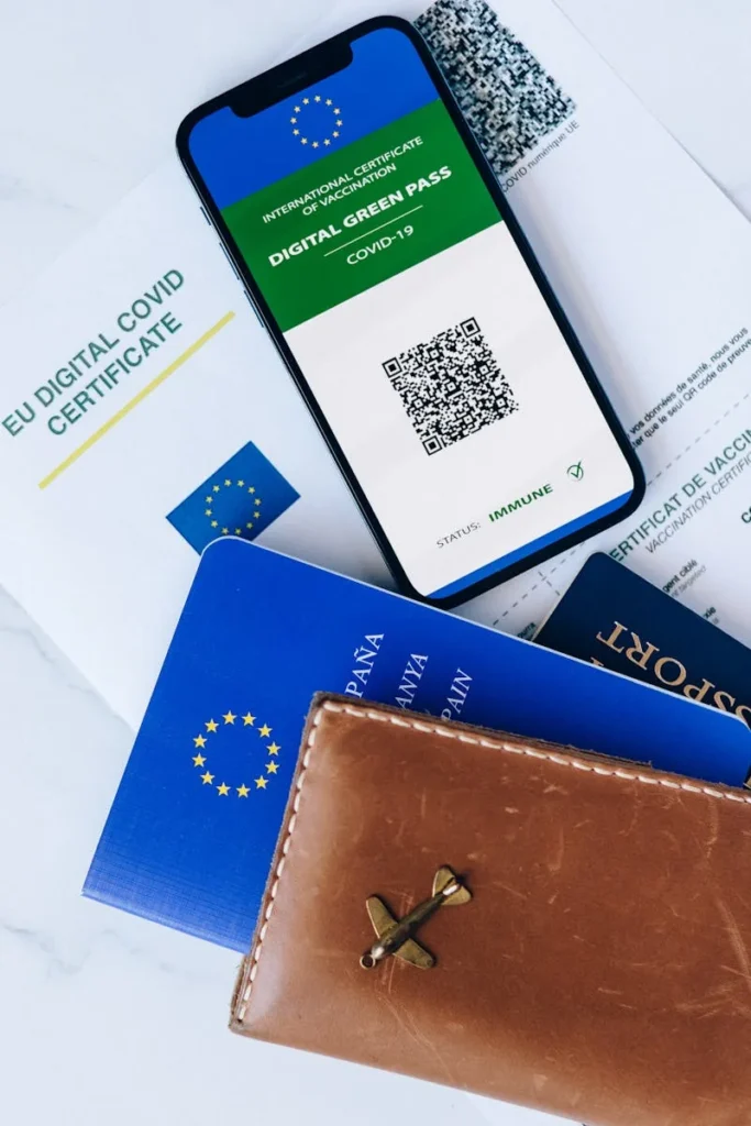 Still life of a digital COVID certificate, passports, and a leather wallet for travel documentation.